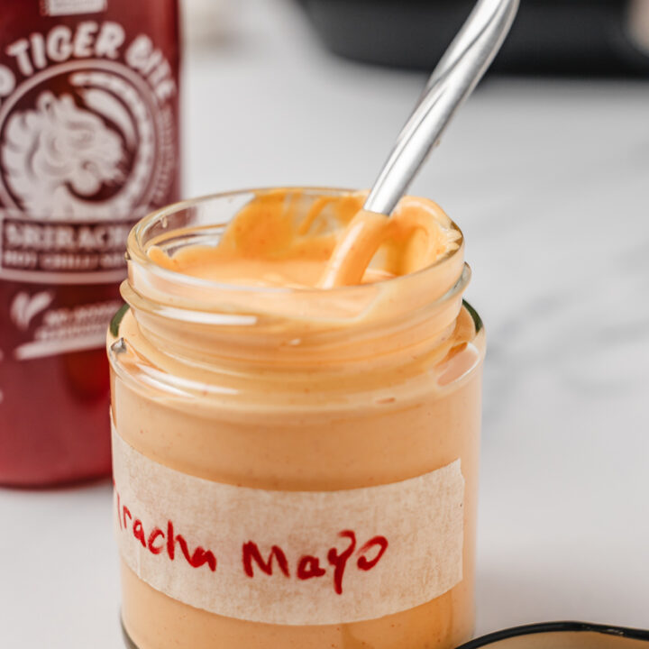opened sriracha mayo in a jar with a spoon in it.