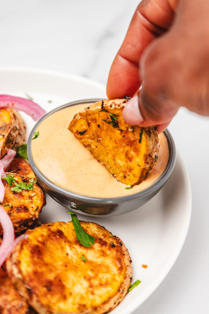 a hand dipping potato slice in a dipping sauce.